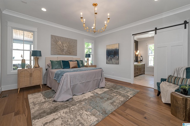 bedroom with crown molding, an inviting chandelier, connected bathroom, hardwood / wood-style floors, and a barn door