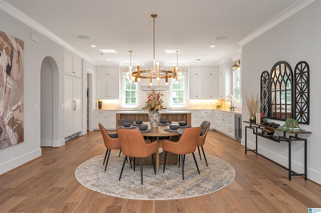 dining space featuring beverage cooler, light hardwood / wood-style floors, crown molding, and an inviting chandelier