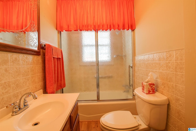 full bathroom featuring tile walls, vanity with extensive cabinet space, toilet, and enclosed tub / shower combo