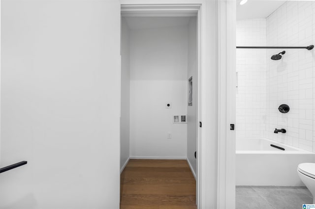 bathroom featuring wood-type flooring, tiled shower / bath combo, and toilet