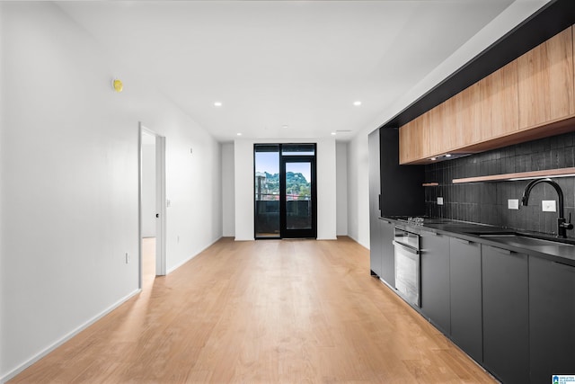 kitchen with oven, light hardwood / wood-style floors, backsplash, and sink