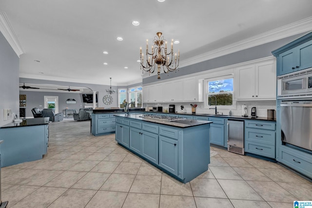 kitchen with blue cabinets, appliances with stainless steel finishes, a center island, ceiling fan with notable chandelier, and white cabinetry