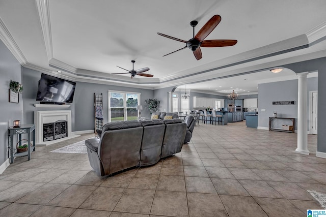 tiled living room with ceiling fan with notable chandelier, crown molding, decorative columns, and a tray ceiling