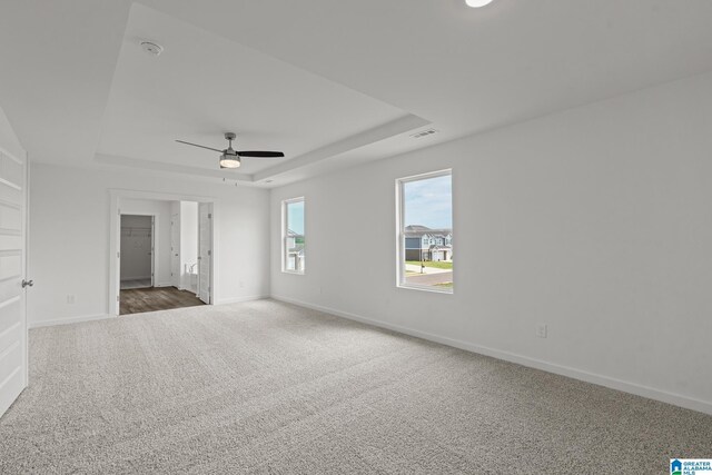 spare room featuring dark colored carpet, a tray ceiling, visible vents, and baseboards