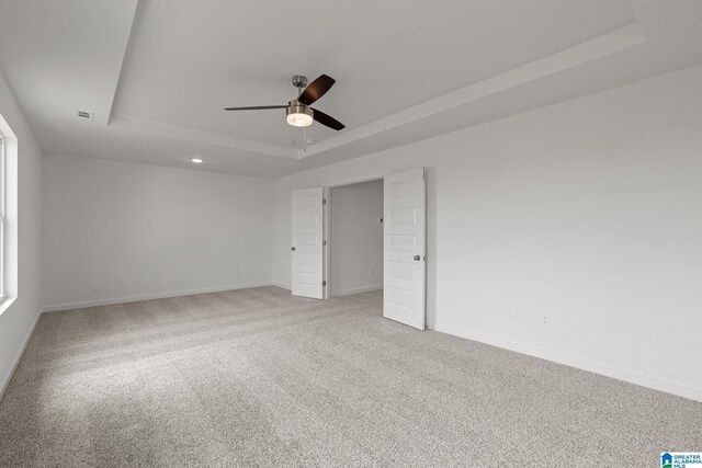 spare room with visible vents, baseboards, a raised ceiling, a ceiling fan, and light colored carpet