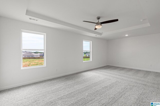 carpeted empty room featuring a ceiling fan, a raised ceiling, a wealth of natural light, and baseboards