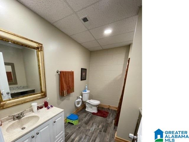 bathroom featuring a drop ceiling, toilet, vanity, and hardwood / wood-style floors