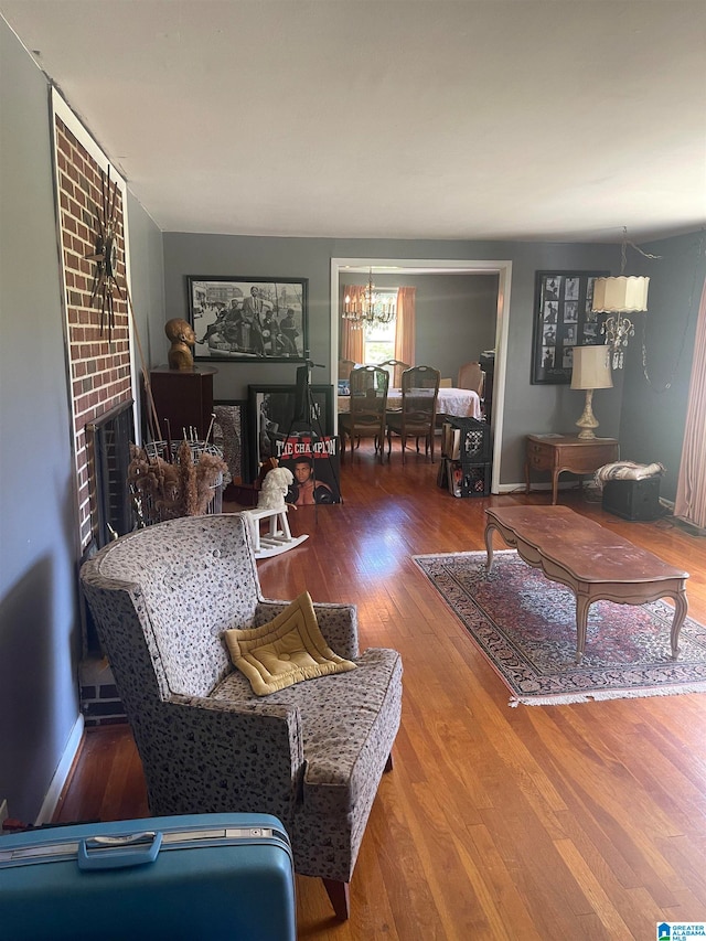 living room featuring brick wall, a chandelier, hardwood / wood-style flooring, and a brick fireplace