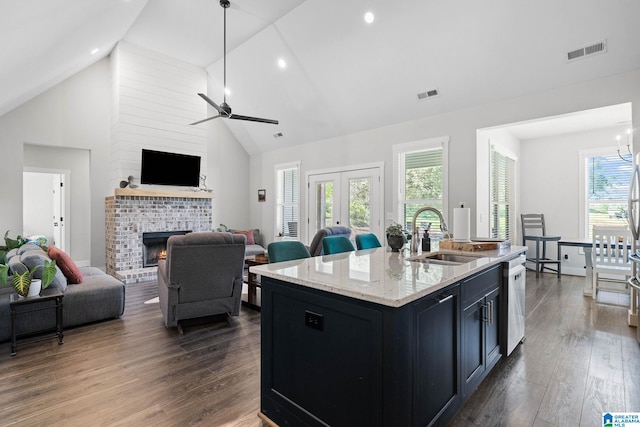 kitchen with high vaulted ceiling, a brick fireplace, a center island with sink, dark wood-type flooring, and sink