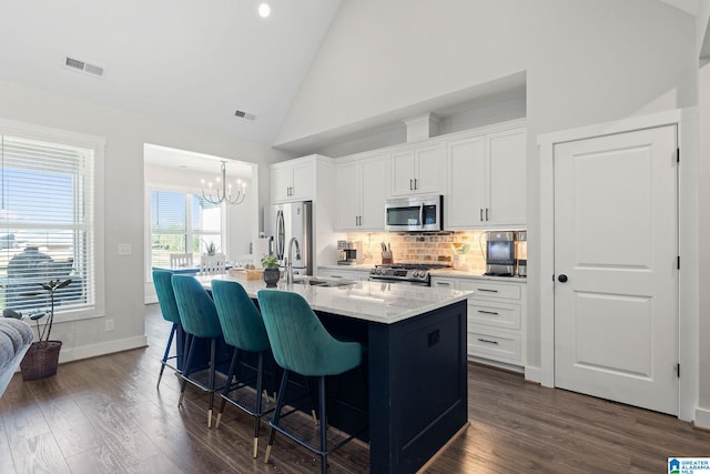 kitchen with appliances with stainless steel finishes, sink, white cabinetry, dark wood-type flooring, and a kitchen island with sink