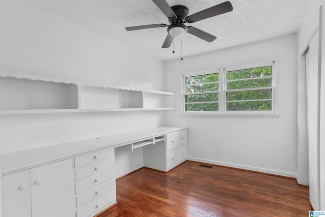 unfurnished office featuring dark hardwood / wood-style floors, built in desk, ceiling fan, and a textured ceiling