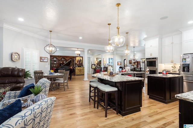 kitchen featuring light hardwood / wood-style floors, decorative columns, a breakfast bar area, and a center island with sink