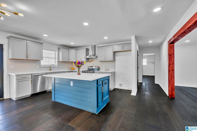 kitchen with backsplash, stainless steel appliances, a kitchen island, dark wood-type flooring, and wall chimney range hood