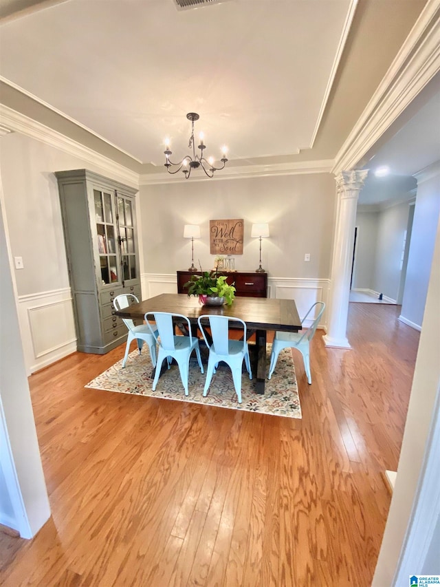 dining space featuring decorative columns, crown molding, a notable chandelier, and light hardwood / wood-style flooring