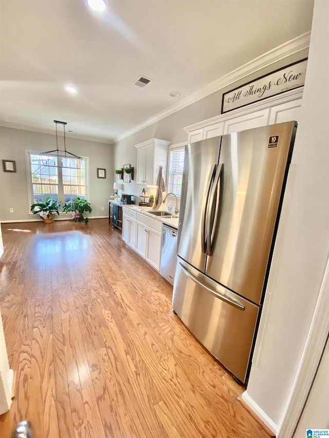 kitchen with appliances with stainless steel finishes, light wood-type flooring, crown molding, white cabinets, and hanging light fixtures