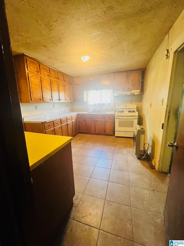 kitchen with a textured ceiling, white range with gas cooktop, and light tile floors