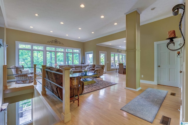 living room featuring plenty of natural light, ornamental molding, light wood-type flooring, and ornate columns