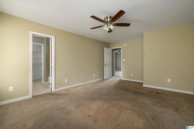 unfurnished bedroom with light carpet, a walk in closet, ceiling fan, and ensuite bath