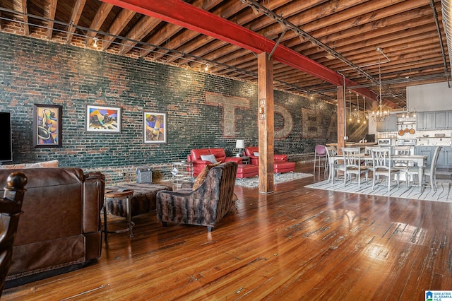 living room with beamed ceiling, a towering ceiling, hardwood / wood-style flooring, and brick wall