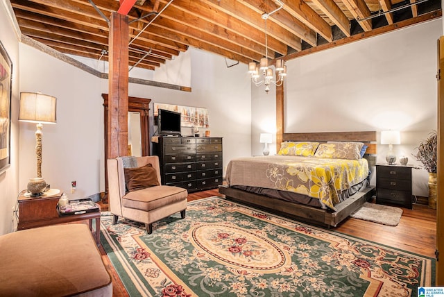 bedroom featuring wood-type flooring, a high ceiling, and beam ceiling