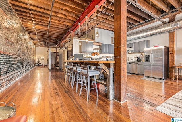 kitchen with stainless steel appliances, gray cabinetry, brick wall, and hardwood / wood-style floors