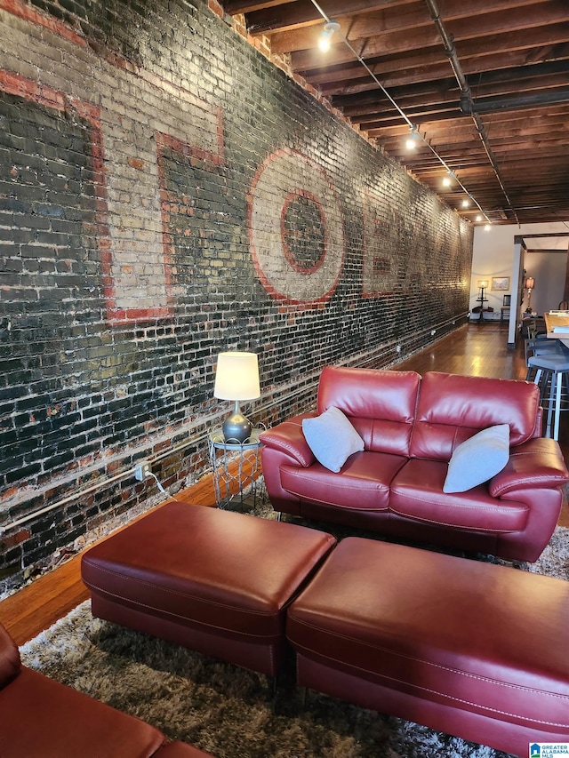 living room featuring rail lighting, hardwood / wood-style flooring, and brick wall