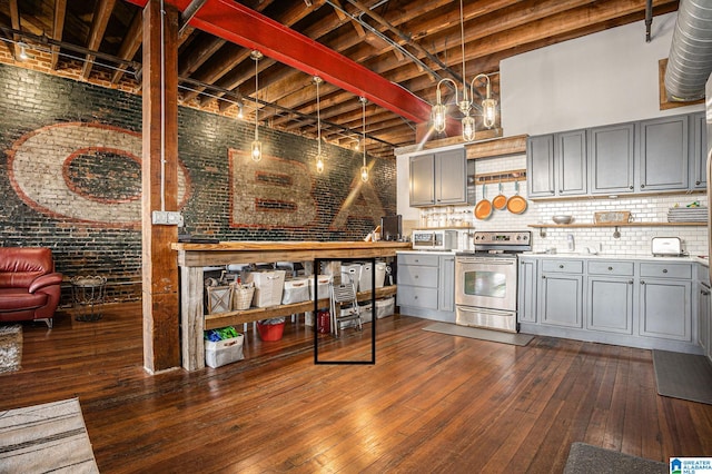 kitchen featuring electric range, dark wood-type flooring, brick wall, and gray cabinetry