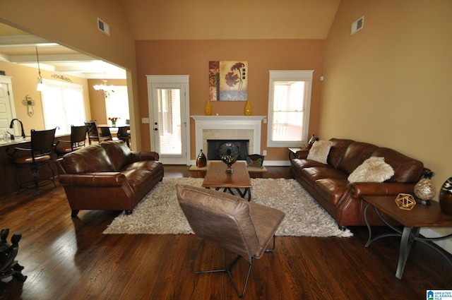 living room featuring high vaulted ceiling, hardwood / wood-style flooring, a tiled fireplace, and a chandelier