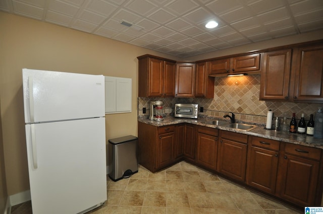 kitchen with light tile floors, white fridge, sink, backsplash, and dark stone countertops