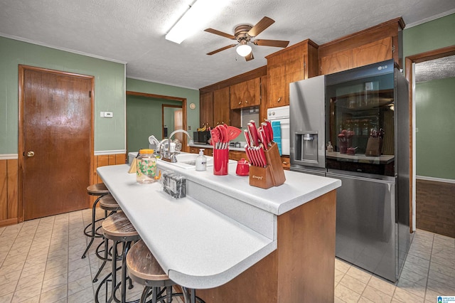 kitchen featuring light tile floors, stainless steel fridge with ice dispenser, white oven, ceiling fan, and an island with sink