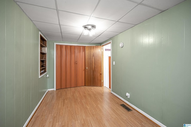 interior space featuring built in shelves, light hardwood / wood-style floors, and a paneled ceiling