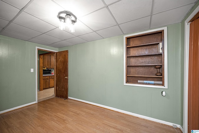 unfurnished room featuring hardwood / wood-style floors, a paneled ceiling, and built in shelves