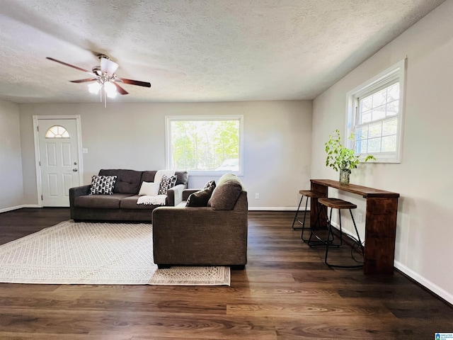 living area with ceiling fan, a wealth of natural light, a textured ceiling, and baseboards