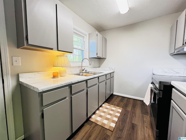 kitchen with dark wood finished floors, light countertops, black range with electric stovetop, a sink, and gray cabinetry