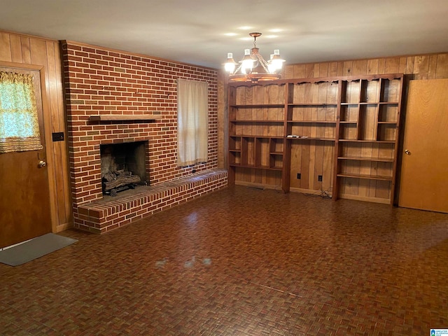 unfurnished living room with a fireplace, an inviting chandelier, and wood walls