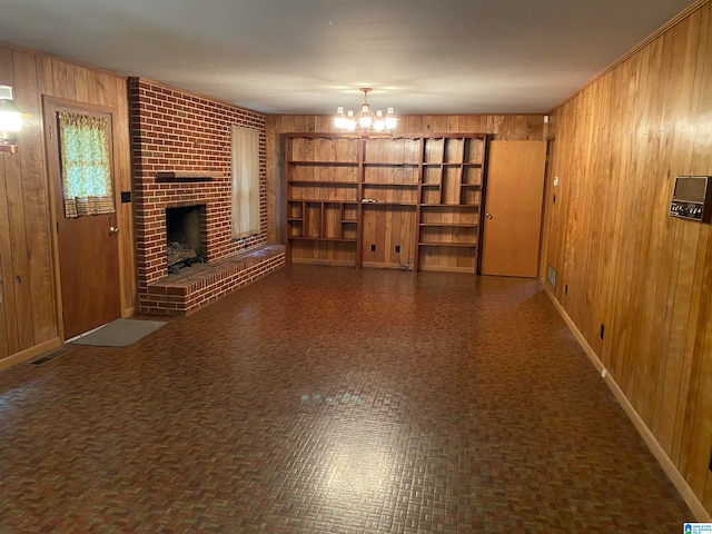 unfurnished living room with wooden walls, a fireplace, and a notable chandelier