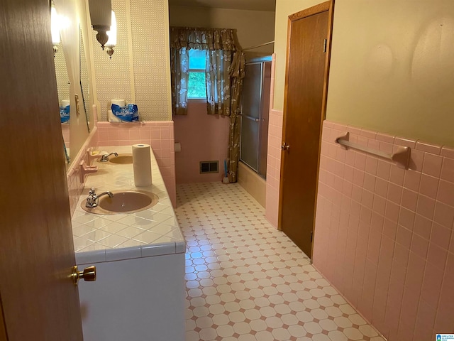 bathroom featuring combined bath / shower with glass door, vanity, and tile walls