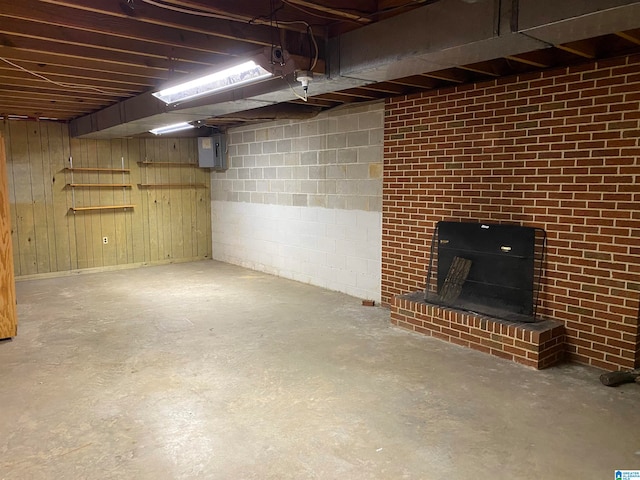 basement with electric panel, wood walls, and a fireplace