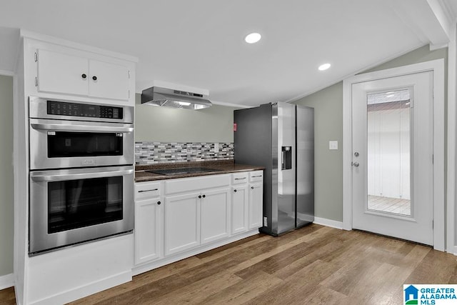 kitchen with backsplash, extractor fan, stainless steel appliances, vaulted ceiling, and hardwood / wood-style flooring