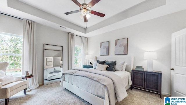 bedroom with multiple windows, ceiling fan, and a tray ceiling