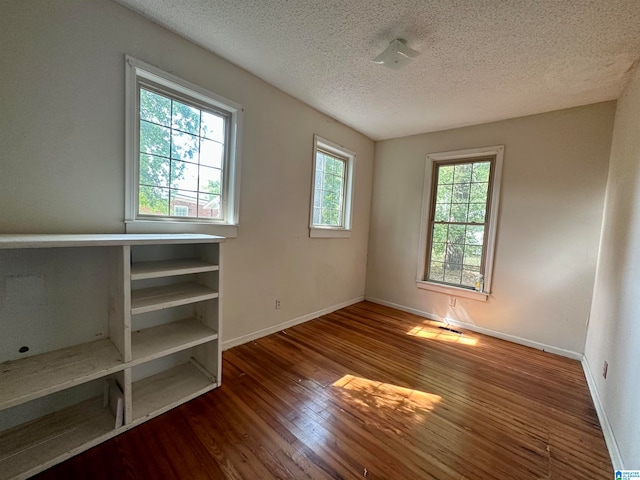 spare room featuring a healthy amount of sunlight, hardwood / wood-style flooring, and a textured ceiling