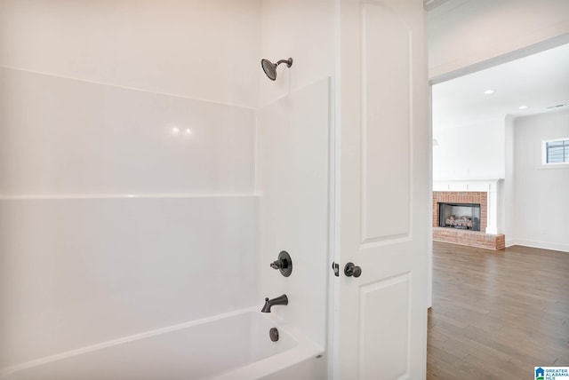 bathroom featuring shower / bath combination, hardwood / wood-style floors, and a brick fireplace