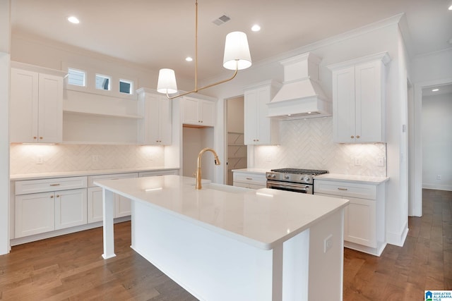 kitchen with white cabinetry, high end range, an island with sink, and custom range hood