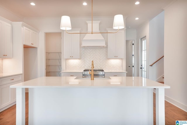 kitchen featuring pendant lighting, premium range hood, a center island with sink, and white cabinets