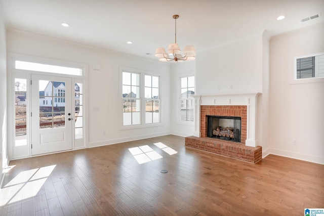 unfurnished living room featuring crown molding, a brick fireplace, an inviting chandelier, and light hardwood / wood-style flooring