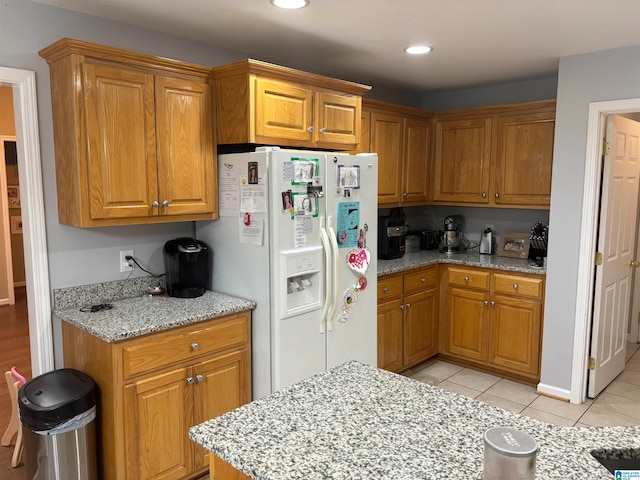 kitchen featuring white fridge with ice dispenser, light stone counters, and light tile floors