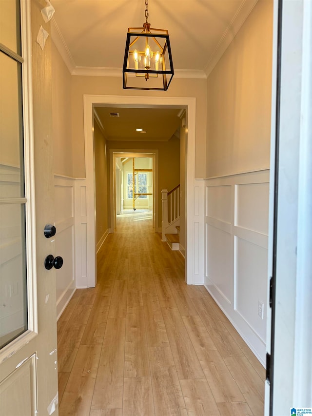 hall featuring crown molding, light hardwood / wood-style floors, and an inviting chandelier