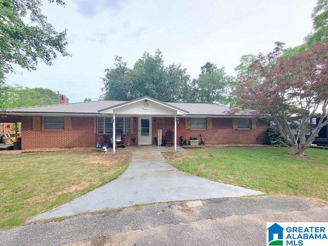 single story home featuring concrete driveway, brick siding, a chimney, and a front yard