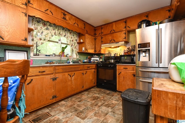 kitchen with a sink, black appliances, brown cabinets, and under cabinet range hood