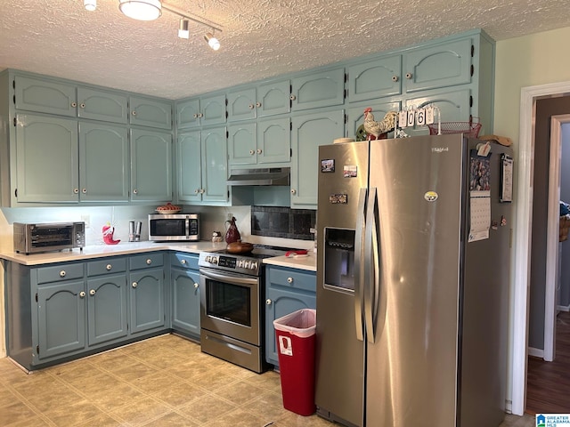 kitchen with a textured ceiling, appliances with stainless steel finishes, blue cabinetry, rail lighting, and tasteful backsplash